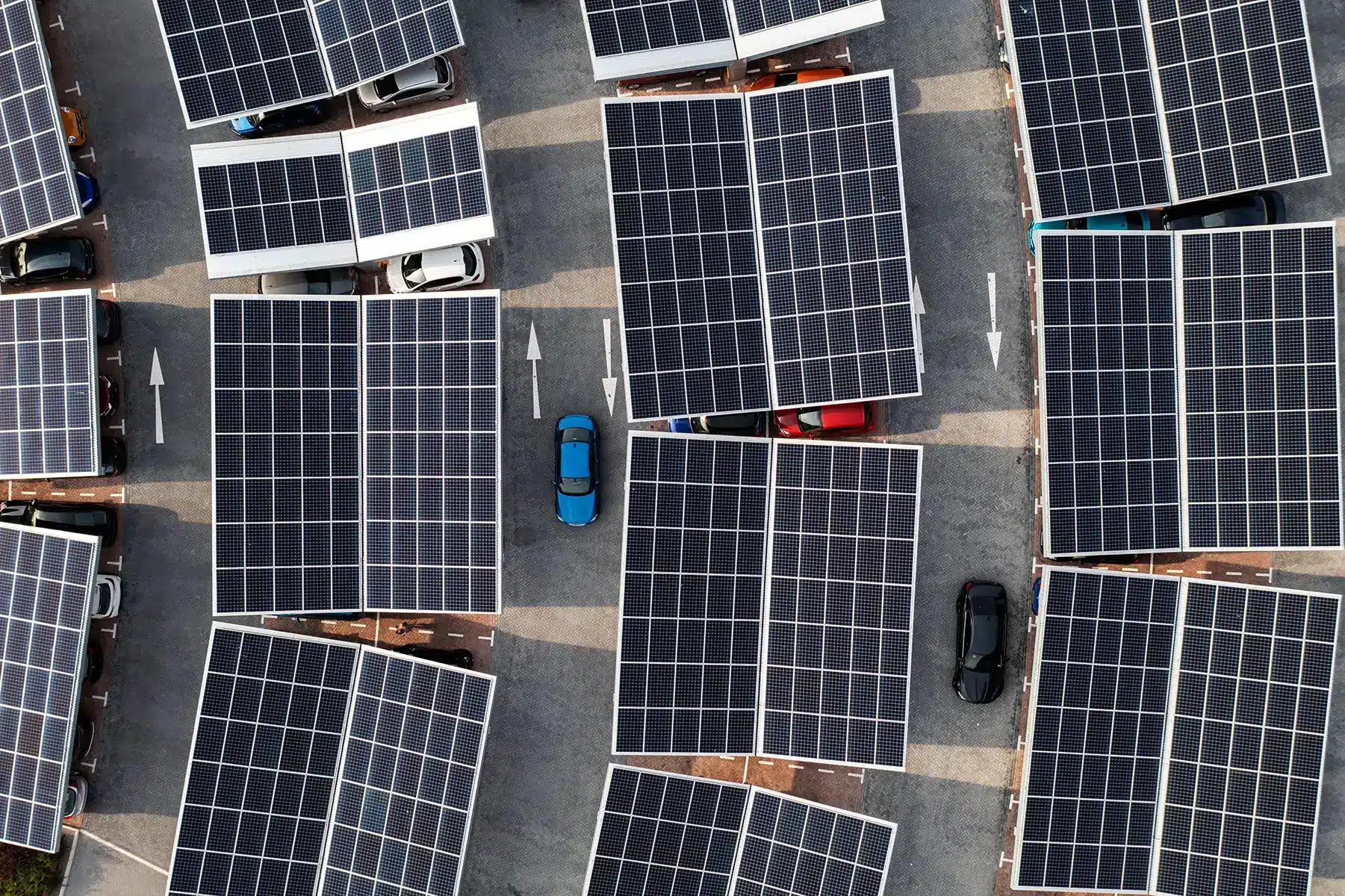 Aerial view directly above electric cars parking under solar panels on a parking lot rooftop ready for charging